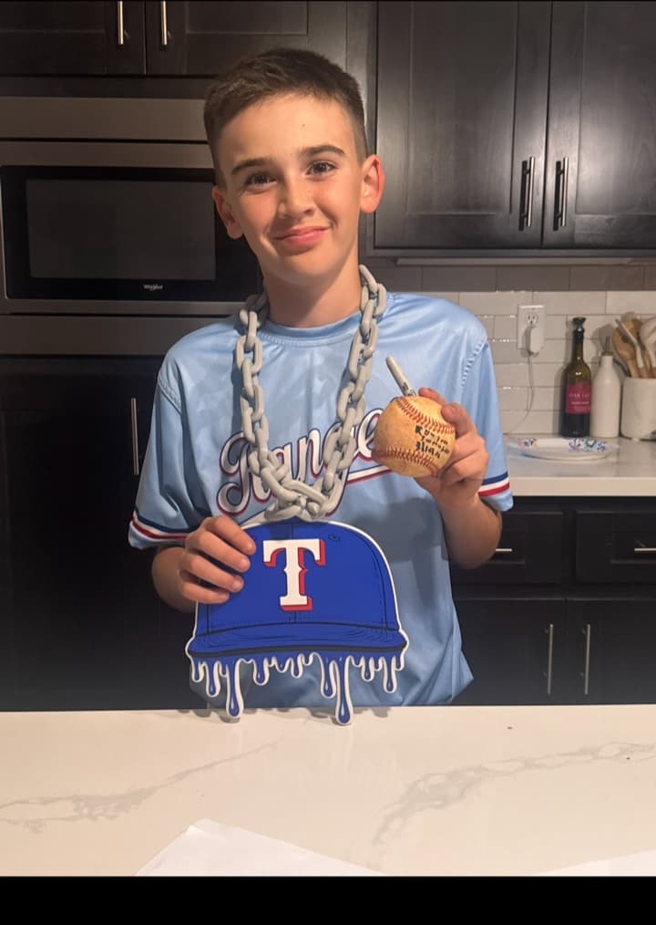 Young baseball player holding a signed ball and wearing a custom blue cap-shaped hype chain