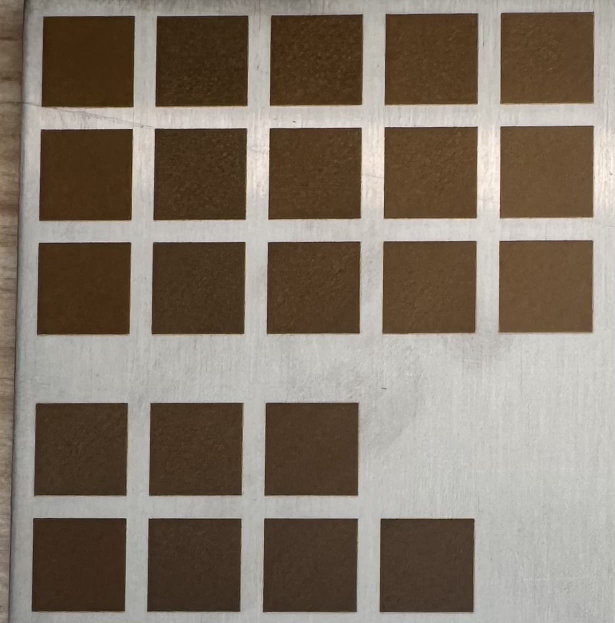 Post-burn overview photo of the LAB-0002 24-cell test grid on a 304 stainless mirror-finish coupon