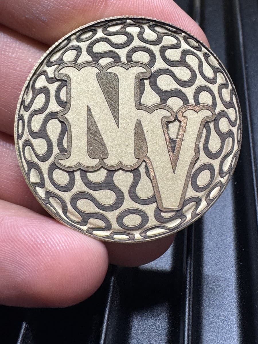 Engraved round medallion with NV lettering and repeating pattern