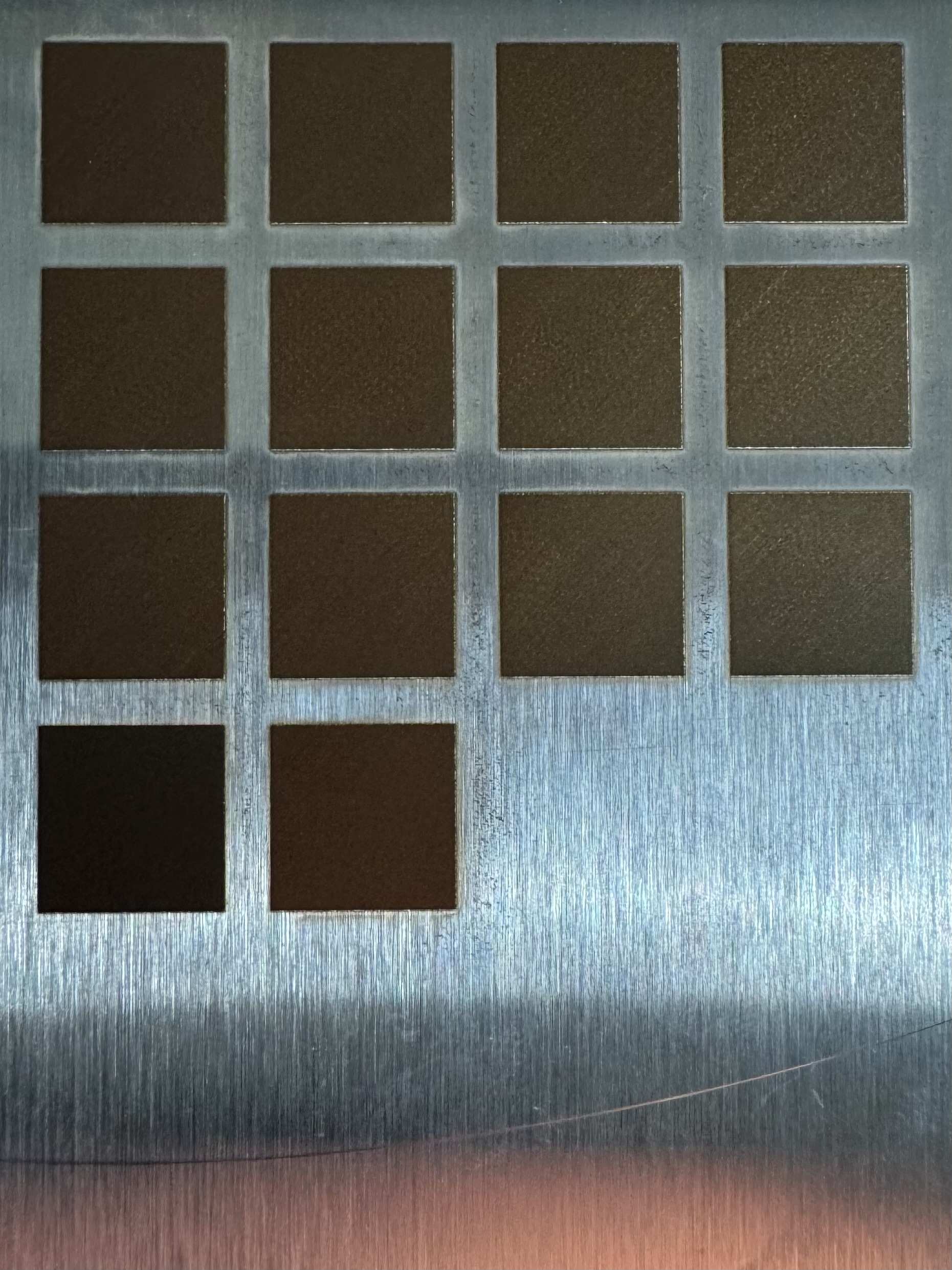 Post-burn photograph of the LAB-0006 identical-recipe control grid on a 304 stainless steel coupon, showing a visible lightness gradient across the field